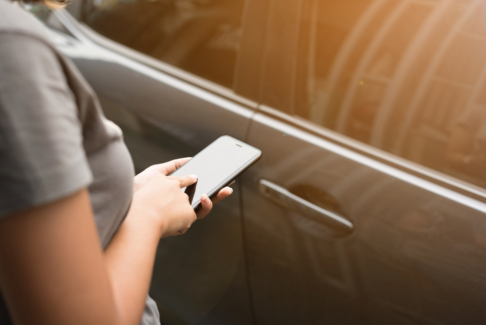 Woman using smartphone in front of vehicle.